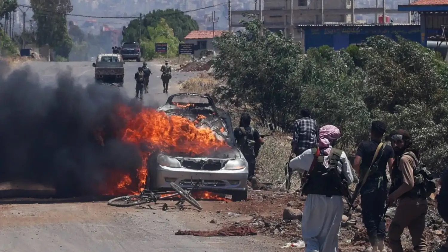 مقاتلون من العشائر ينتشرون في الوقت الذي تحترق فيه سيارة عند المدخل الغربي لمدينة السويداء معقل الدروز في سوريا