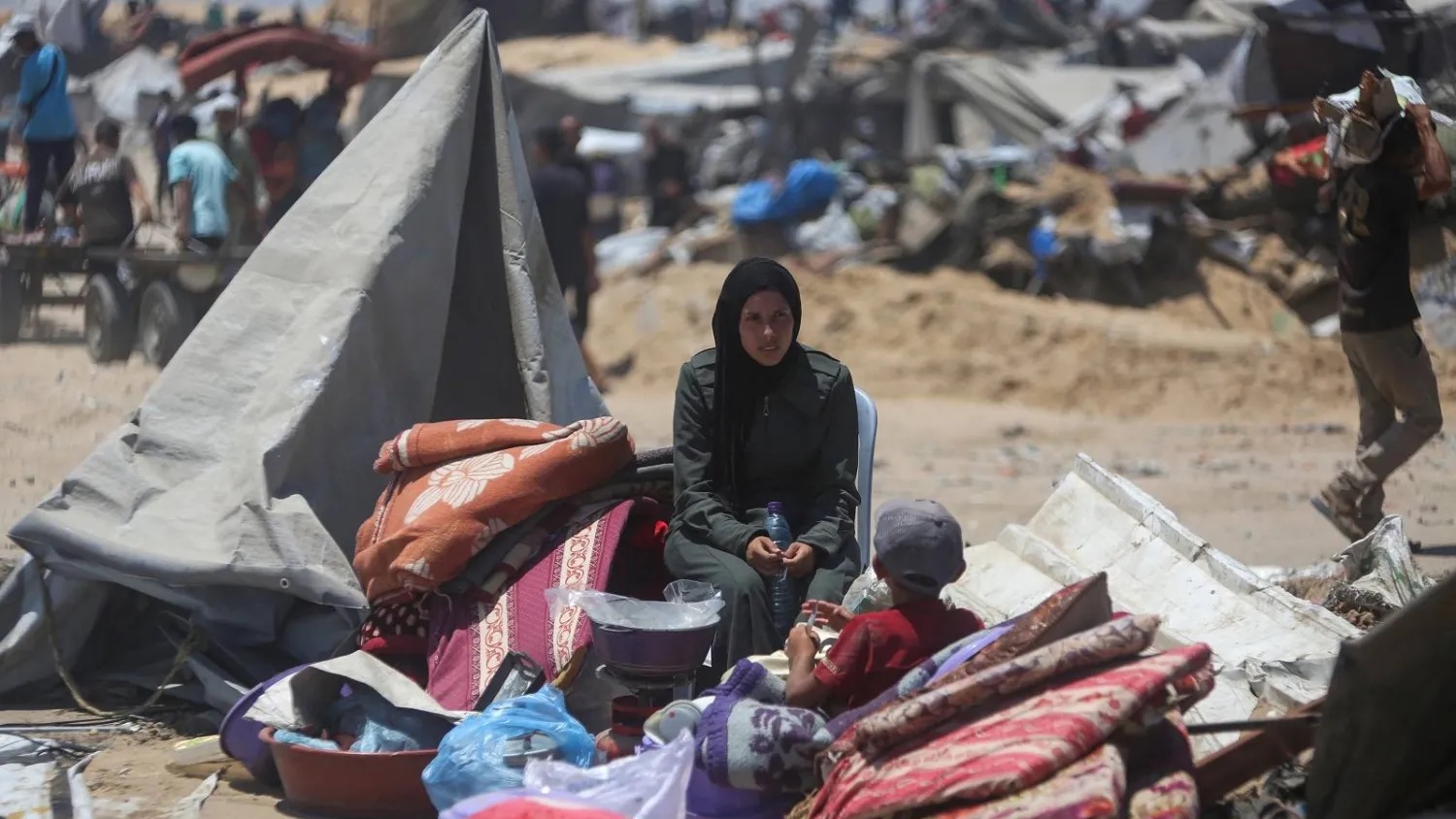 امرأة وطفل يجلسان على متعلقات تم إنقاذها بينما يتفقد فلسطينيون خياماً مدمرة في خان يونس