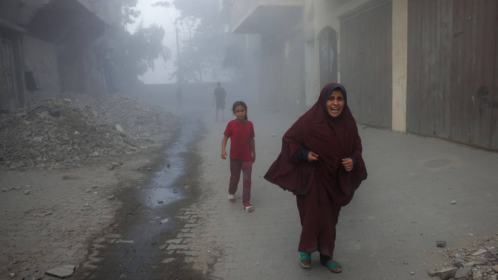 امرأة فلسطينية وأطفالها يهرعون بعيداً عن موقع غارات جوية إسرائيلية على مبنى من ستة طوابق غرب جباليا