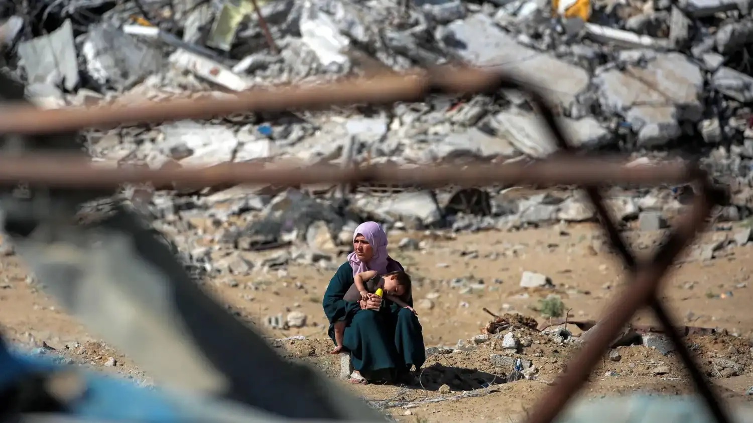 فلسطينية تحمل طفلها وتجلس قرب أكوام من الأنقاض خلال التحرك باتجاه مدينة غزة الجمعة