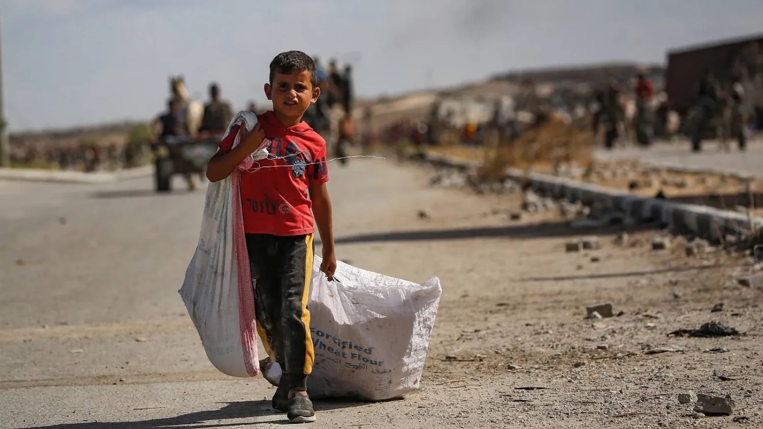 طفل فلسطيني يحمل حقيبة ويجرّ أخرى خلفه بالقرب من معبر نتساريم وسط قطاع غزة