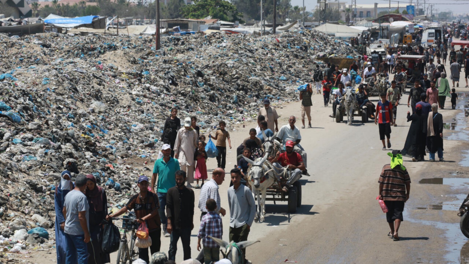 فلسطينيون يسيرون قرب أكوام من النفايات في خان يونس بجنوب قطاع غزة في 18 تموز (يوليو) 2024