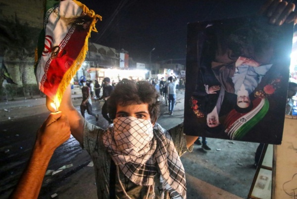 متظاهر عراقي يحمل علما إيرانيا وشخص آخر يضرم النار فيه خلال احتجاجات البصرة