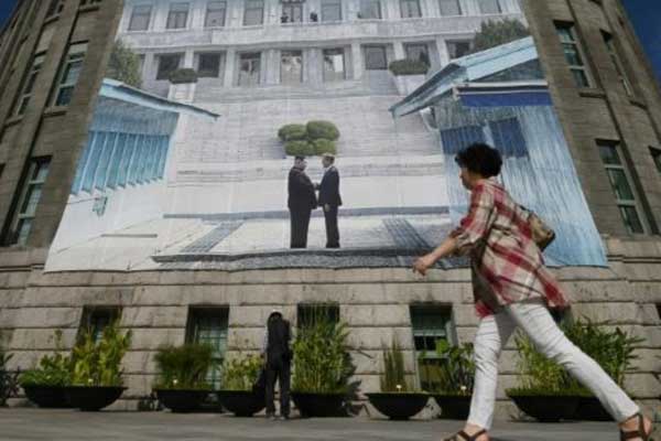 سيدة تمر في 13 سبتمبر أمام ملصق عملاق وسط سيول لصورة من قمة سابقة للرئيسين الكوري الشمالي والكوري الجنوبي اللذين سيلتقيان مجددًا في 18 سبتمبر 2018