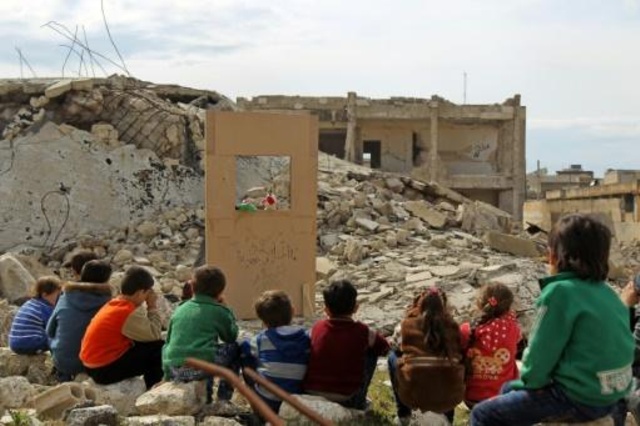 أطفال يشاهدون عرضاً للدمى وسط الدمار في 27 آذار/مارس 2019 في مدينة سراقب في محافظة إدلب في شمال غرب سوريا