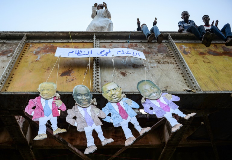 سودانيون فوق جسر يعلقون دمى ورقية تظهر وجوه عدة مسؤولين سابقين بينهم الرئيس الأسبق عمر البشير كتب فوقها 