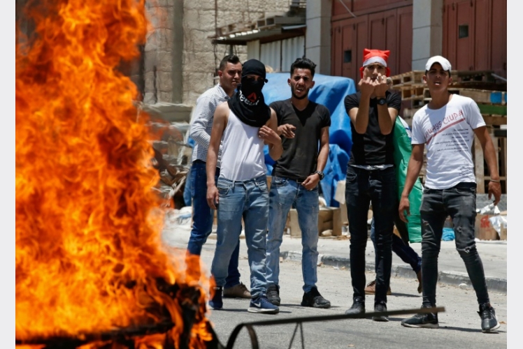 فلسطينيون يحملون حجارة خلف اطارات مشتعلة خلال مواجهة بعد مسيرة احتجاج ضد ورشة البحرين