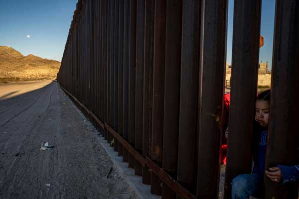 فتاة مكسيكية تقف عند الجدار المعدني الفاصل بين الولايات المتحدة والمكسيك في أنابرا في ولاية نيو مكسيكو الأميركية، في 19 مارس 2019