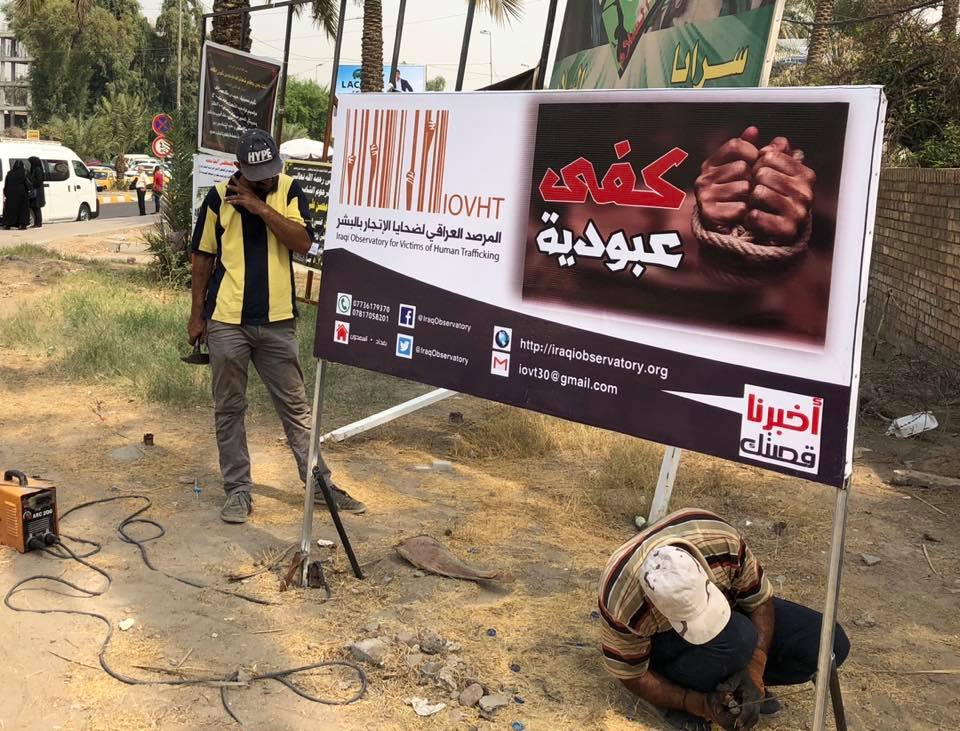 نشطاء المرصد العراقي لضحايا الإتجار بالبشر يعلقون لوحة تناهض العبودية أمام جامعة بغداد في 2018