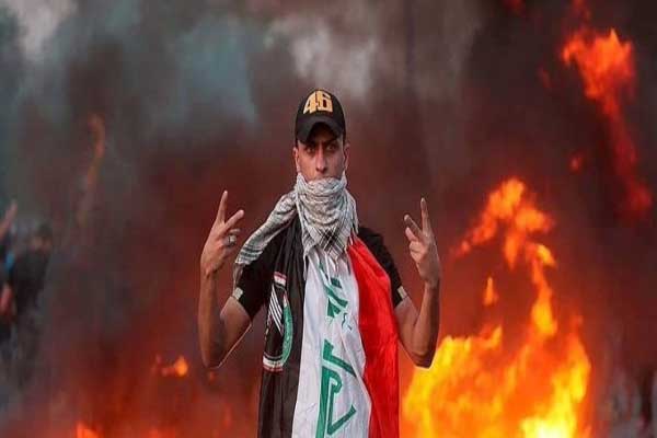 متظاهر في الناصرية وخلفه أحد مقار الأحزاب السياسية وقد اشتعلت فيه النيران