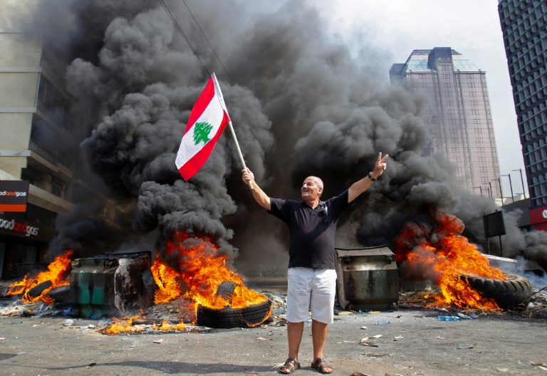متظاهر يلوح بالعلم اللبناني امام اطارات محروقة في 18 تشرين الاول/اكتوبر 2019 في العاصمة بيروت.
