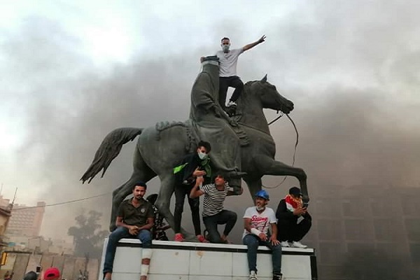 متظاهرون يعتلون تمثالا للملك فيصل الأول - أول ملوك العراق قرب مكتب عبد المهدي