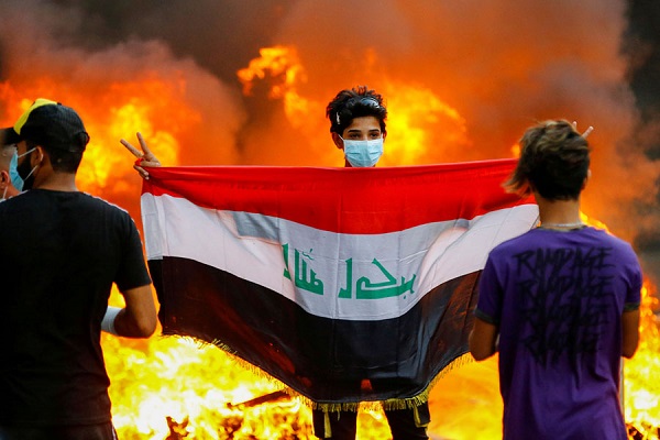 متظاهر يرفع العلم العراقي ونيران هجوم الأمن خلفه