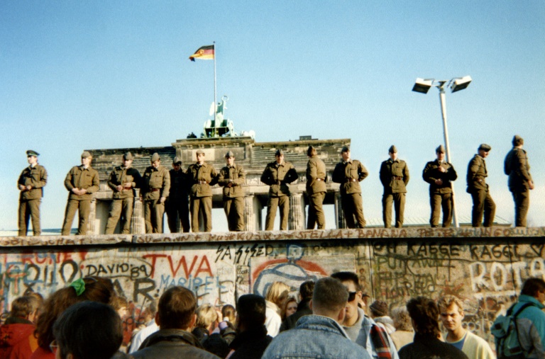 حرس حدود من المانيا الشرقية سابقا يقفون على قسم من جدار برلين وتبدو بوابة براندنبورغ خلفهم في 11 نوفمبر 1989