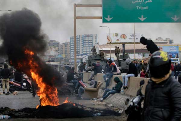 متظاهرون قطعوا طريقًا رئيسًا مؤديًا إلى مدينة طرابلس في شمال لبنان في 25 نوفمبر 2019 تلبية لدعوة إلى إضراب عام واحتجاجًا على التأخير في تشكيل حكومة جديدة