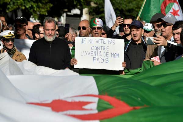 محتجون جزائريون يسيرون حاملين أعلامًا وطنية ولافتات أثناء تظاهرة معارضة للانتخابات الرئاسية في العاصمة الجزائر في 10 ديسمبر 2019