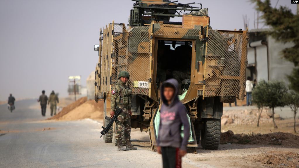 جندي سوري يقف بجانب مدرعة على الطريق السريع بالقرب من مدينة عين عيسى شرقي سوريا