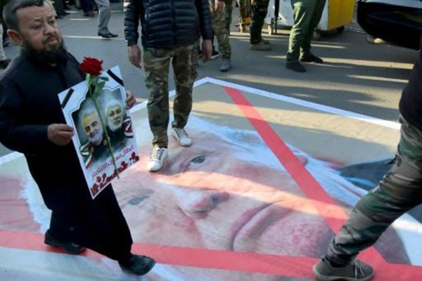 عراقي يسير فوق صورة للرئيس الأميركي دونالد ترمب خلال تكريم قوات الحشد الشعبي للجنرال الإيراني قاسم سليماني الذي اغتالته واشنطن