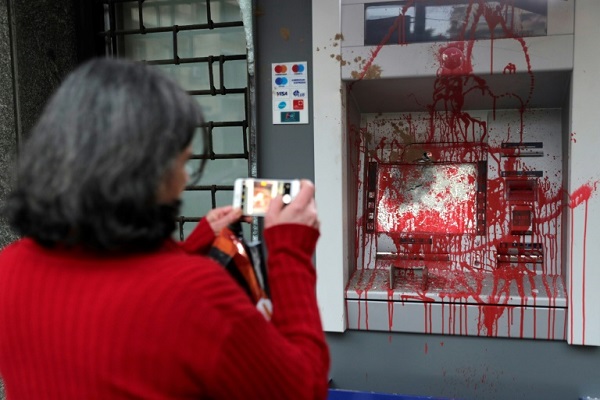 سيدة تلتقط في 15 يناير 2020 صورة لصراف آلي رشّه المتظاهرون بالطلاء الأحمر