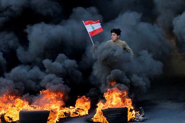 فتى يحمل العلم اللبناني وسط الدخان الأسود المنبعث من إطارات مشتعلة أحرقها المتظاهرون في 14 يناير 2020 في منطقة جل الديب