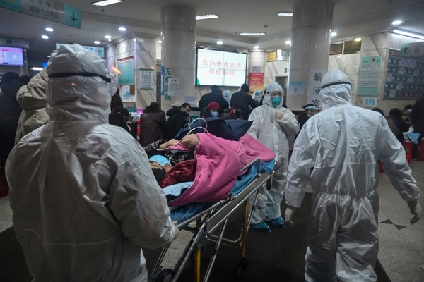 عاملون في المجال الطبي يرتدون بزات للوقاية من فيروس كورونا المستجدّ يصلون مع مريض على سرير متنقل إلى مستشفى الصليب الأحمر في ووهان في وسط الصين في 25 يناير 2020