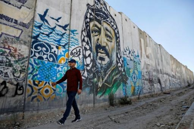 رجل يمشي قرب جدارية تحمل صورة عملاقة للزعيم الفلسطيني الراحل ياسر عرفات على جزء من الجدار الفاصل المثير للجدل الذي بنته إسرائيل 