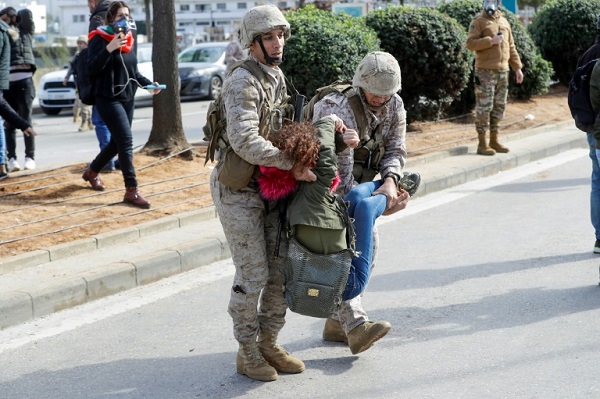 رجلا أمن يحملان متظاهرة معارضة للحكومة خلال تظاهرة احتجاج أمام البرلمان على منح الثقة للحكومة في العاصمة بيروت في 11 فبراير 2020.