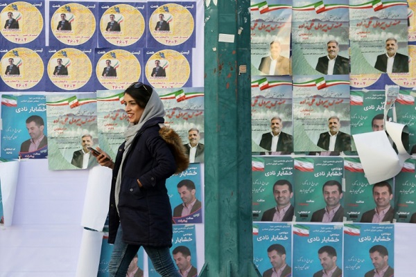 ايرانية تمر امام جدار عليه ملصقات انتخابية في أحد شوارع طهران في 18 فبراير 2020