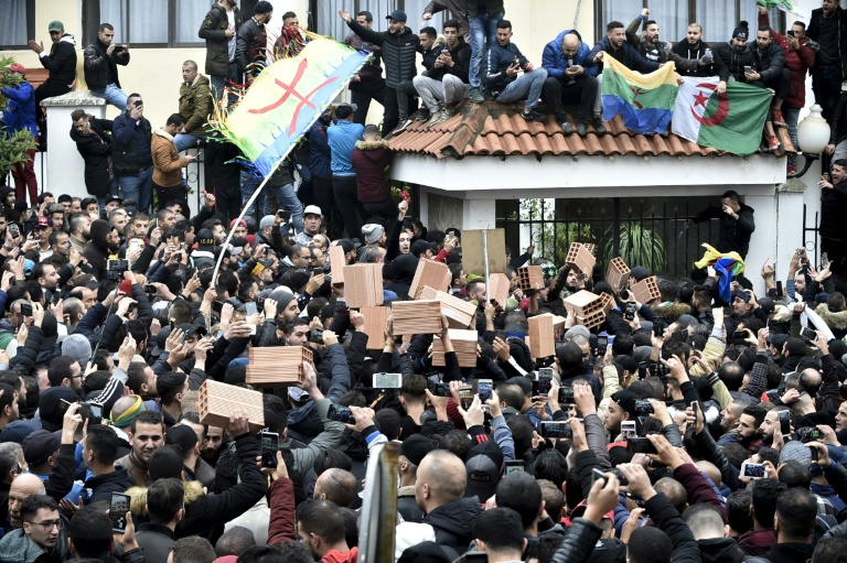 متظاهرون يلوحون بالأعلام الجزائرية والأمازيغية ويرفعون الطوب، في تجمع في تيزي وزو، إحدى المدن الرئيسية في منطقة القبائل (شمال)، في 8 كانون الأول/ديسمبر 2019