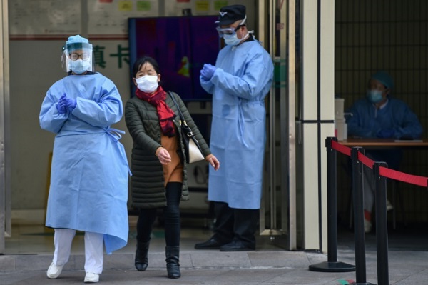 امرأة ترتدي قناعاً تعبر بين موظفين في مستشفى في شنغهاي في 27 فبراير 2020