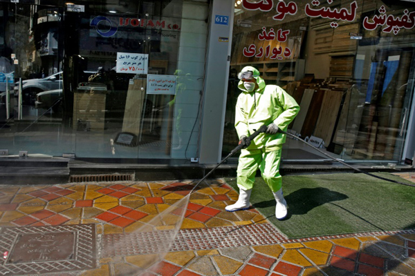 عنصر دفاع مدني إيراني وعمال بلديون يعملون على تعقيم طريق في العاصمة طهران من فيروس كوفيد-19، 5 مارس 2020.