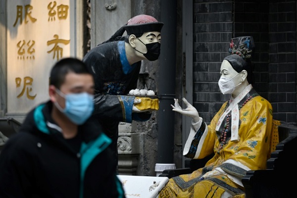 تمثالان وضع على وجهيهما قناعان واقيان عند مدخل مطعم على طول شارع تجاري في بكين