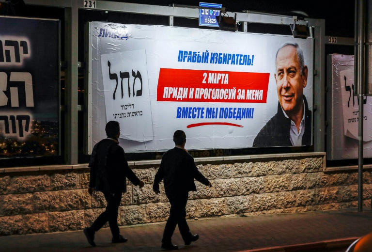 رجلان من اليهود المتشددين يمران من أمام لوحة انتخابية دعائية باللغة الروسية تحمل صورة رئيس الوزراء الإسرائيلي بنيامين نتانياهو في القدس في 27 شباط/فبراير 2020
