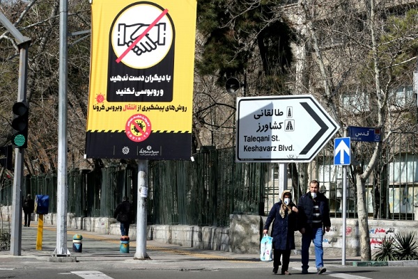 ايرانيون يرتدون أقنعة واقية ويسيرون بجانب لافتة تدعو الى الوقاية من فيروس كورونا في العاصمة طهران