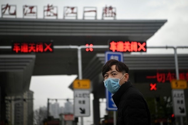 رجل يرتدي قناعاً واقياً يقف أمام معبر مغلق على جسر جيوجيانغ شانغجيانغ المؤدي إلى مقاطعة هوباي في وسط الصين في 6 مارس 2020