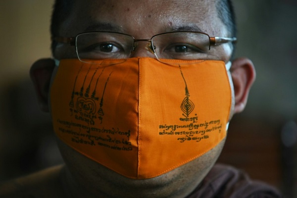 راهب بوذي يرتدي قناعاً واقياً مصنعاً من أغطية العبوات البلاستيكية المعاد تدويرتها في معبد في ساموت براكان في وسط تايلاند في 23 مارس 2020