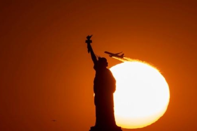 طائرة تحلق خلف تمثال الحرية عند الغروب في نيويورك في 14 ت1/أكتوبر 2019.