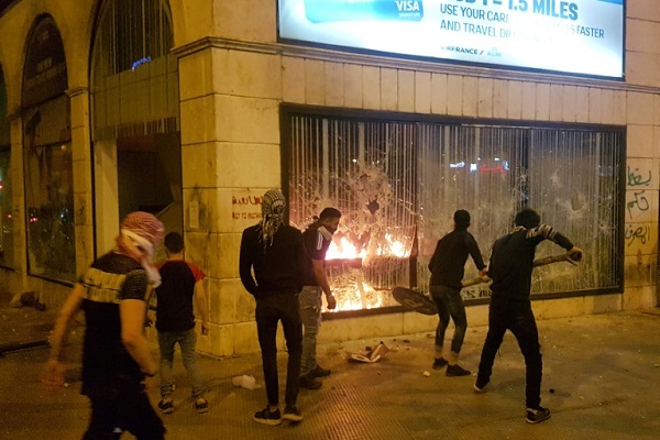 متظاهرون يكسرون عبر إشارة سير واجهة أحد المصارف في مدينة طرابلس في شمال لبنان