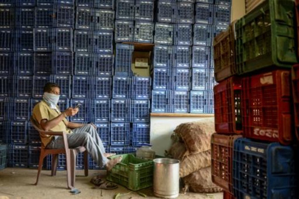 عامل يضع منديلًا على وجهه وينظر إلى هاتفه أثناء استراحة في يوم عيد العمال في سوق لبيع الخضر في حيدر أباد في الهند في الأول من مايو 2020