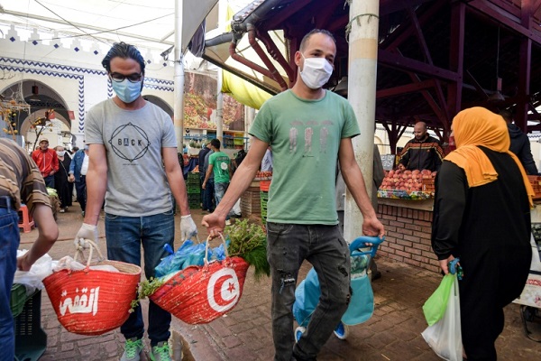 متطوعان تونسيان يرتديان كمامة يوزعان مساعدات غذائية في سوق تونس المركزية