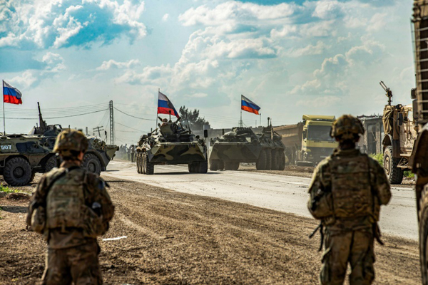 جنود أميركيون يقفون مقابل حاملات جنود روسية في محافظة الحسكة السورية بتاريخ 2 مايو 2020