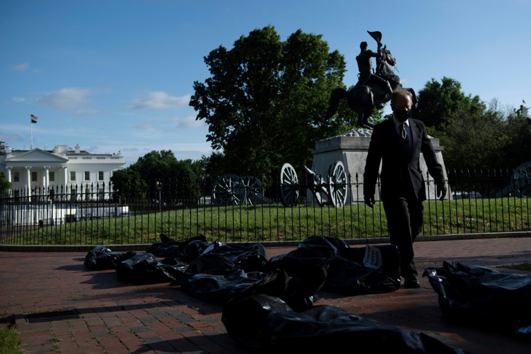 ناشط يسير وسط أكياس تستخدم للفّ الجثث وضعت أمام البيت الأبيض في واشنطن احتجاجاً على طريقة تعامل إدارة الرئيس دونالد ترامب مع أزمة كوفيد-19 في 20 ايار/مايو 2020.