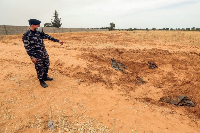 عضو من قوّات الأمن التّابعة لوزارة الداخليّة في حكومة الوفاق الوطني الليبيّة يُشير إلى موقع يُشتبه في أنّه مقبرةٌ جماعيَّة في ترهونة، في 11 حزيران/يونيو 2020.