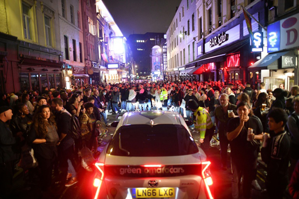  سيارة تحاول العبور بين الساهرين في أحد شوارع حي سوهو في لندن، 4 يوليو 2020