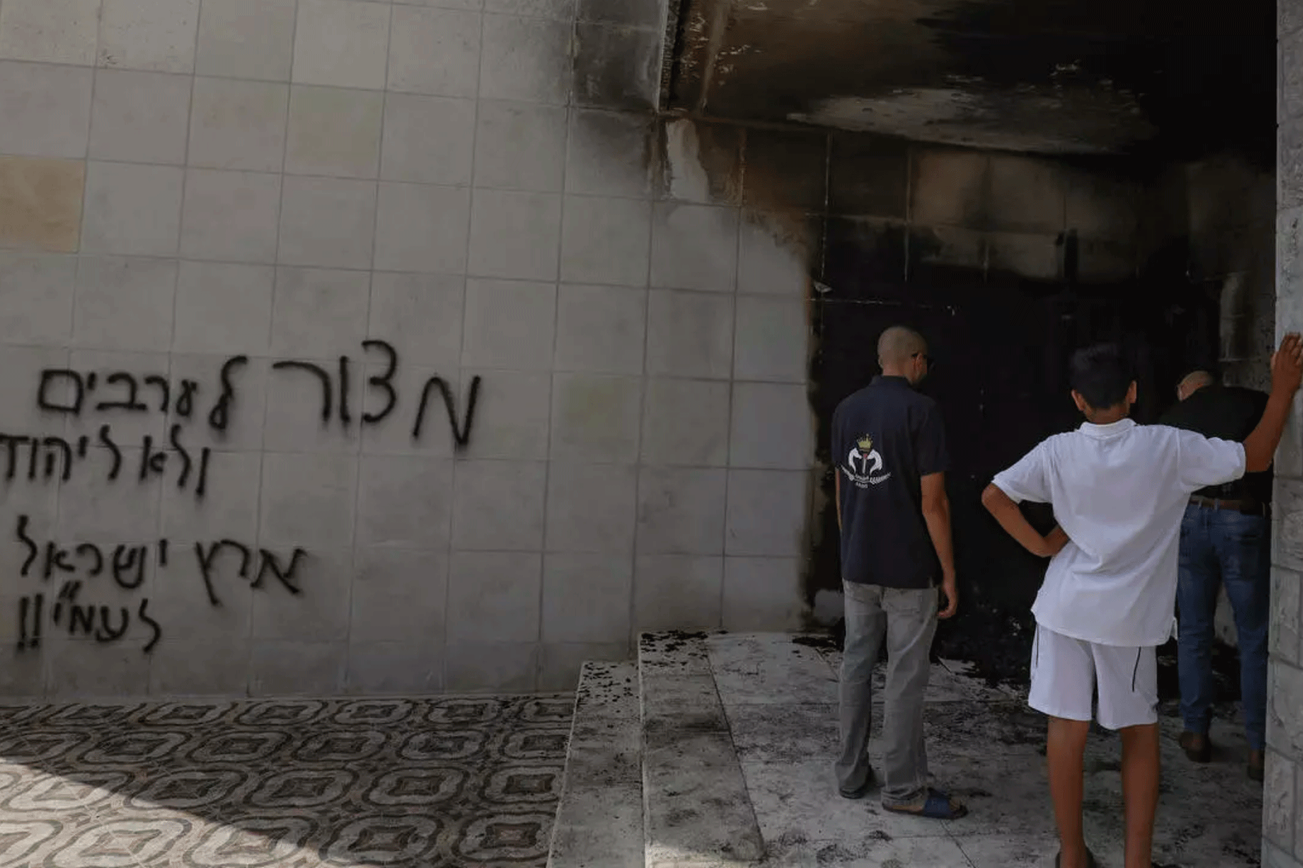 فلسطينيون يعاينون الدمار الذي خلفته نيران أشعلها مستوطنون وشعارات عنصرية خطوها عند مدخل وعلى جدران مسجد في مدينة البيرة في الضفة الغربية المحتلة في 27 يوليو 2020