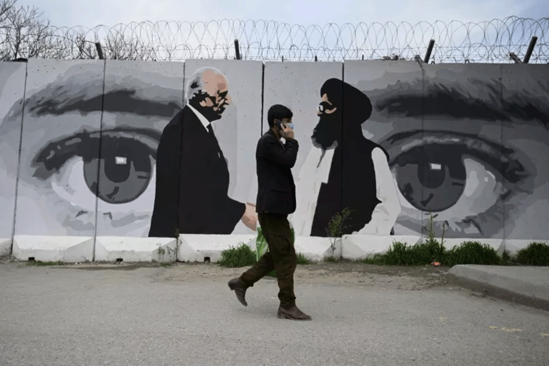 رجل يمر بالقرب من رسم جداري يصور المبعوث الأمريكي الخاص لأفغانستان زلماي خليل زاد (يسار) وونائب الشؤون السياسية لحركة طالبان الملا عبد الغني برادر في كابول، بتاريخ 5 أبريل 2020