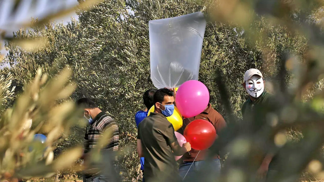 فلسطينيون ملثمون يجهزون بالونات حارقة بالقرب من مخيم البريج للاجئين الفلسطينيين على طول الحدود مع إسرائيل في 12 اغسطس 2020