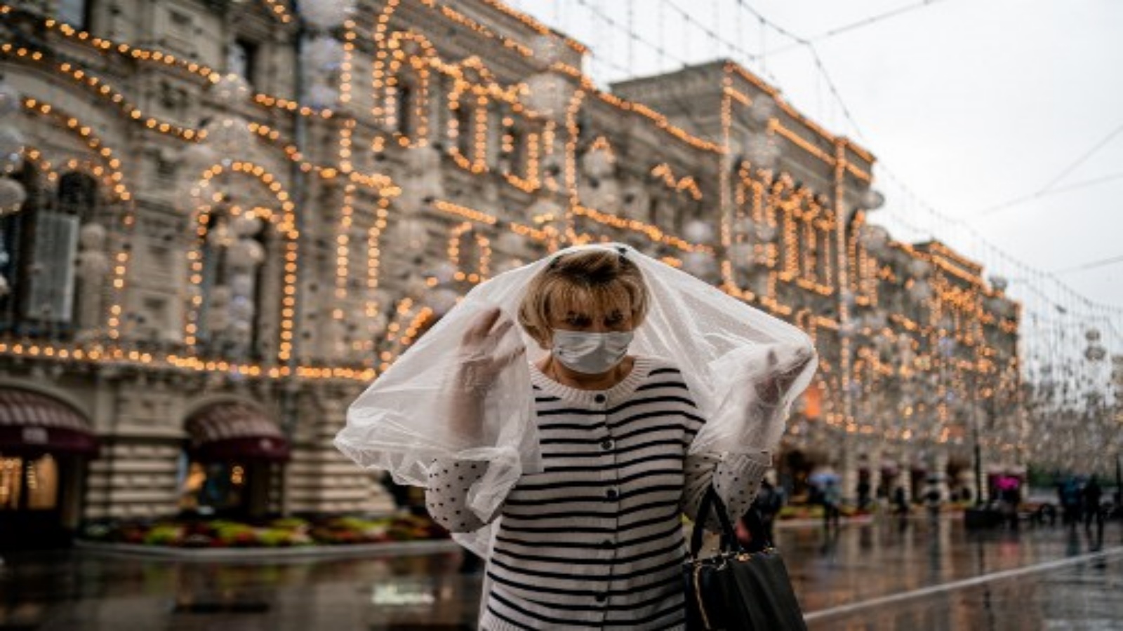 سيدة روسية تتقي المطر بغطاء بلاستك وتتقي كورونا بالكمامة
