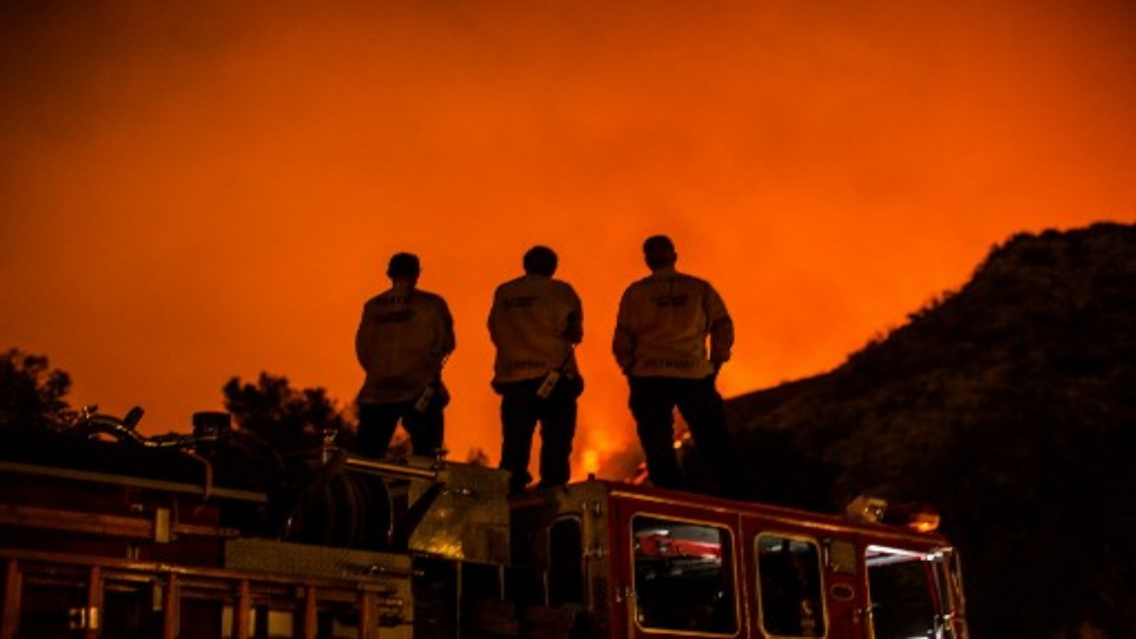 رجال الإطفاء يقفون على شاحنة الإطفاء الخاصة بهم وهم يشاهدون حريق بوبكات يحترق على سفوح التلال خلف المنازل في مونروفيا ، كاليفورنيا في 15 سبتمبر 2020