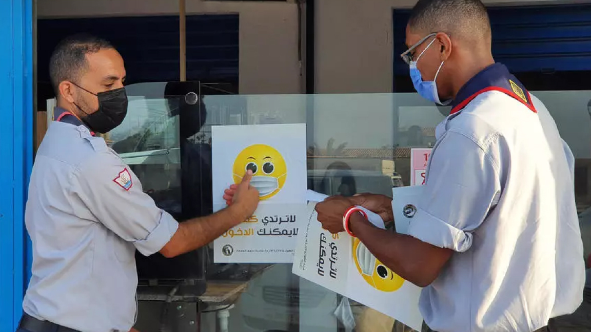 موظفون صحيون ليبيون يضعون ملصفات للتوعية على نافذة متجر في طرابلس في 10 سبتمبر الجاري